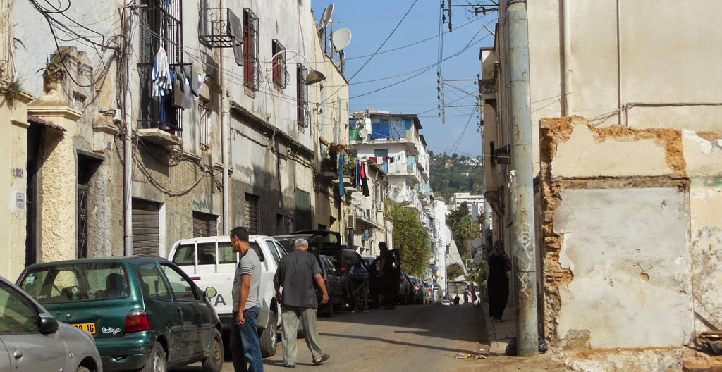 Ruelle populaire d'Alger dans les années 1930, quartier ouvrier baigné de soleil, évoquant l'enfance d'Albert Camus à Belcourt