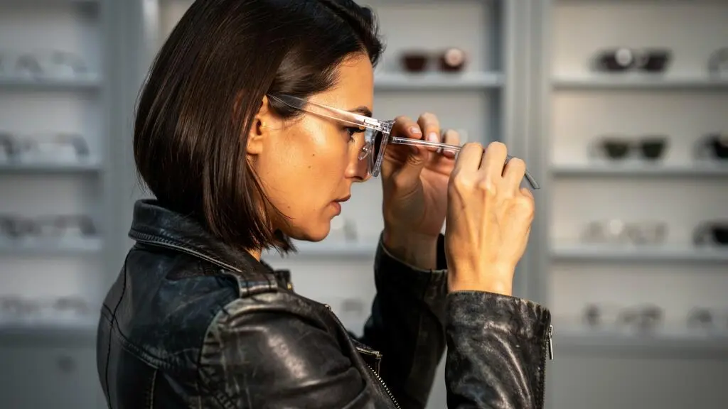 Une femme examine attentivement une monture transparente en boutique d'optique.